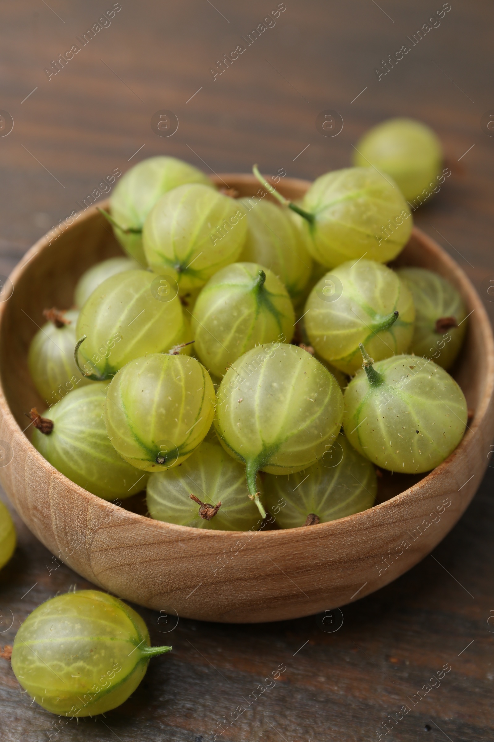 Fresh green gooseberries in bowl on wooden table, closeup Photo of Fresh green gooseberries in bowl on wooden table, closeup