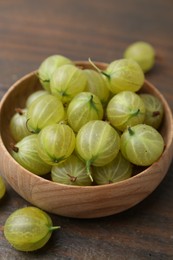 Photo of Fresh green gooseberries in bowl on wooden table, closeup