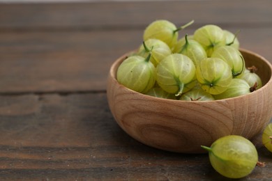 Photo of Fresh green gooseberries in bowl on wooden table, closeup. Space for text