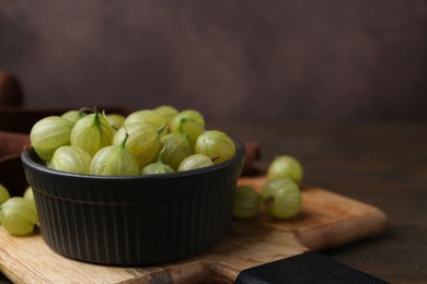Photo of Fresh green gooseberries in bowl on wooden table, closeup. Space for text