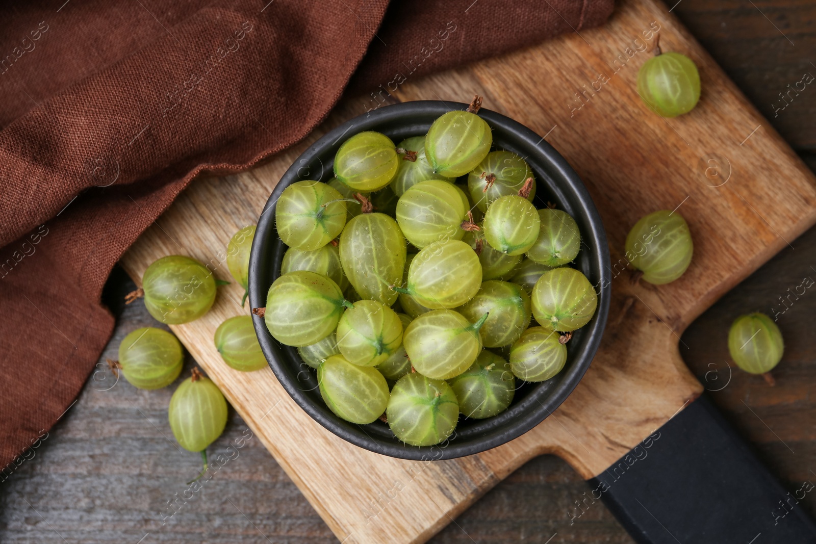 Photo of Fresh green gooseberries in bowl on wooden table, top view