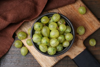 Photo of Fresh green gooseberries in bowl on wooden table, top view