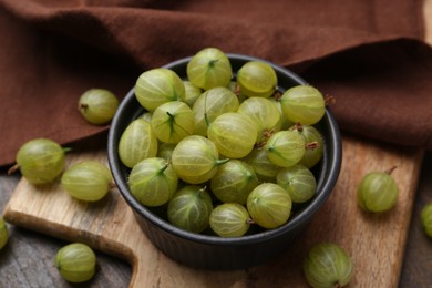 Photo of Fresh green gooseberries in bowl on wooden table, closeup