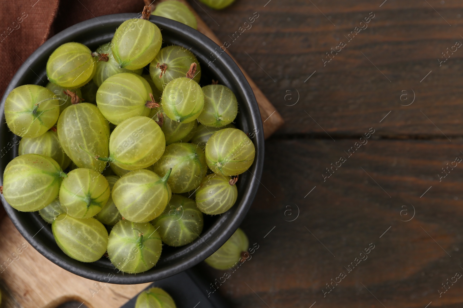 Photo of Fresh green gooseberries in bowl on wooden table, top view. Space for text