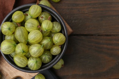 Photo of Fresh green gooseberries in bowl on wooden table, top view. Space for text