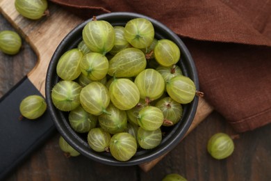 Photo of Fresh green gooseberries in bowl on wooden table, top view