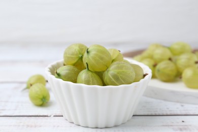 Photo of Fresh green gooseberries in bowl on white wooden table, closeup