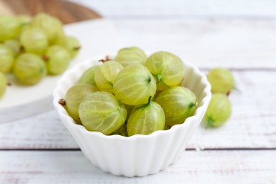 Photo of Fresh green gooseberries in bowl on white wooden table, closeup