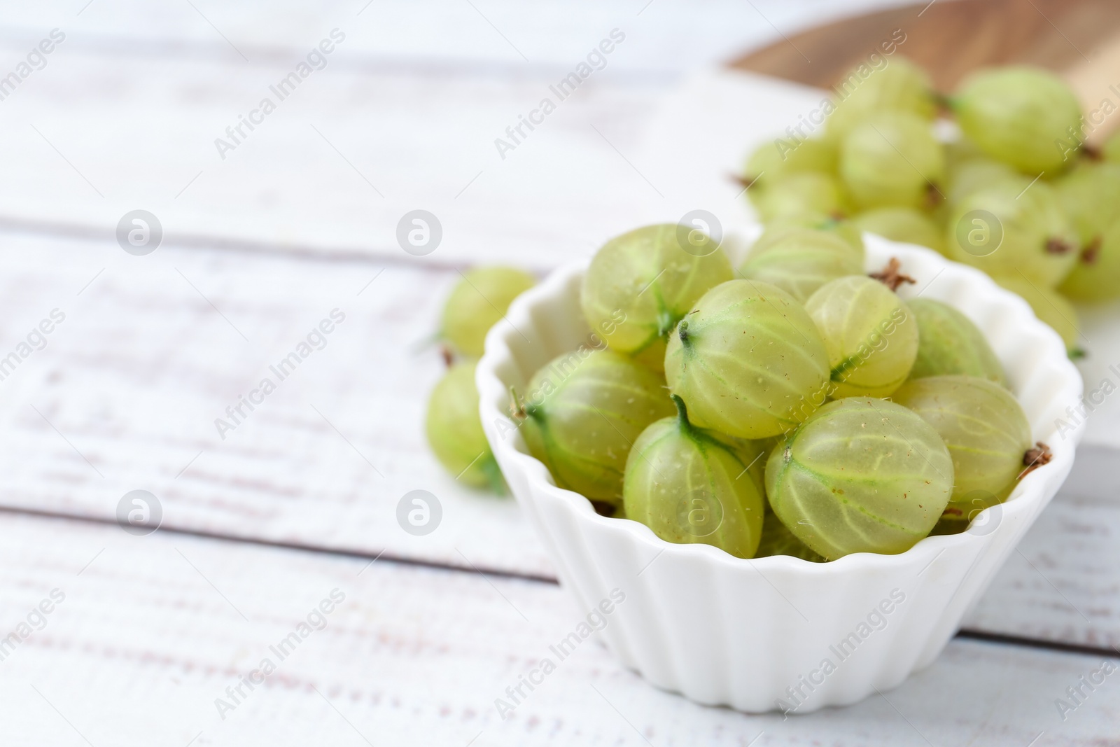 Fresh green gooseberries in bowl on white wooden table, closeup. Space for text Photo of Fresh green gooseberries in bowl on white wooden table, closeup. Space for text