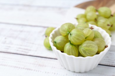 Photo of Fresh green gooseberries in bowl on white wooden table, closeup. Space for text