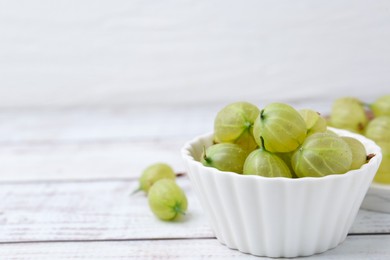 Photo of Fresh green gooseberries in bowl on white wooden table, closeup. Space for text