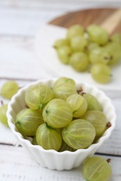 Photo of Fresh green gooseberries in bowl on white wooden table, closeup