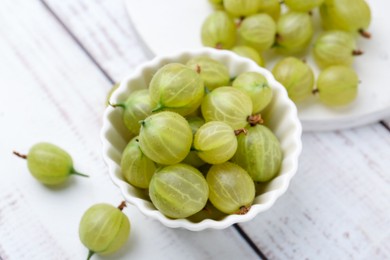Photo of Fresh green gooseberries in bowl on white wooden table, above view