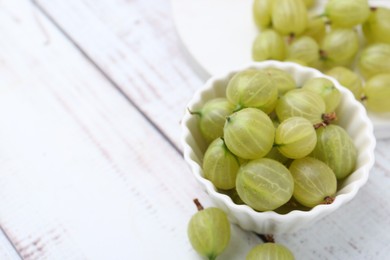 Photo of Fresh green gooseberries in bowl on white wooden table, closeup. Space for text