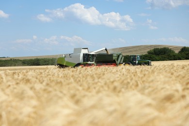 Photo of Combine harvester unloading wheat into tractor trailer in field