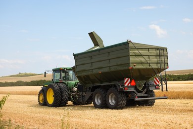 Photo of Modern tractor working in wheat field under blue sky