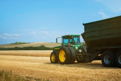 Photo of Modern tractor working in wheat field under blue sky