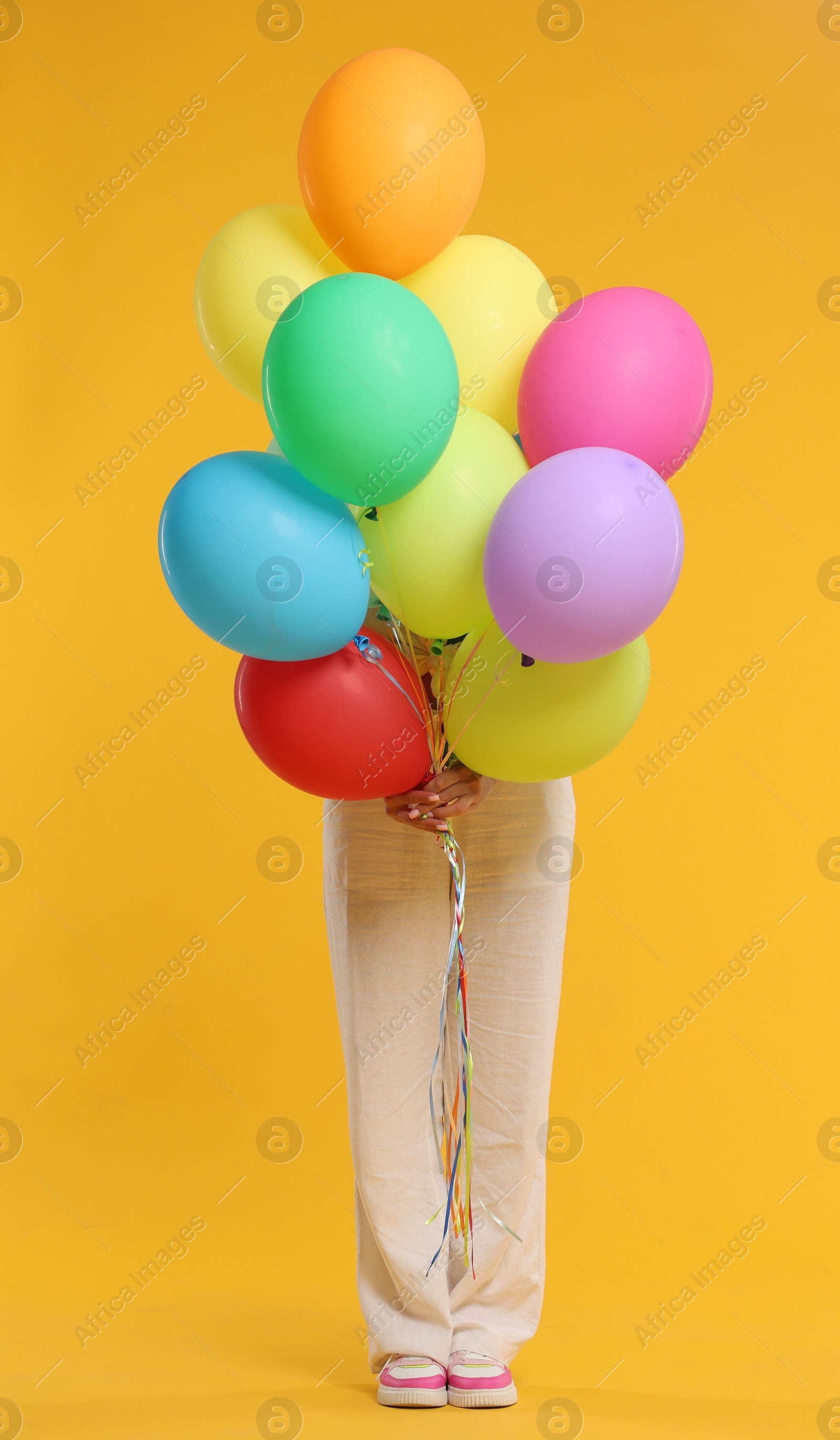 Woman hiding behind bunch of colorful balloons on yellow background Photo of Woman hiding behind bunch of colorful balloons on yellow background