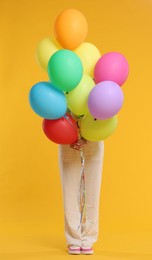 Photo of Woman hiding behind bunch of colorful balloons on yellow background