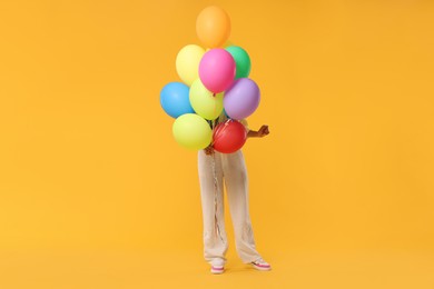 Photo of Woman hiding behind bunch of colorful balloons on yellow background