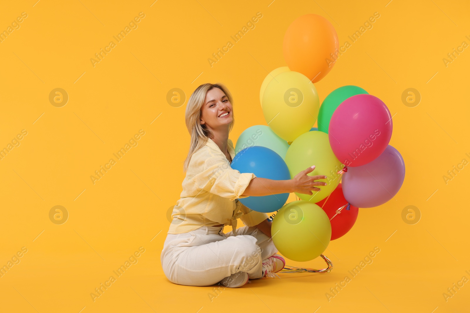 Happy woman with bunch of colorful balloons on yellow background Photo of Happy woman with bunch of colorful balloons on yellow background