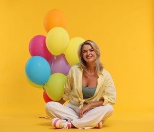Photo of Happy woman with bunch of colorful balloons on yellow background