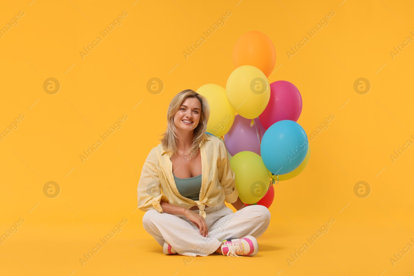 Happy woman with bunch of colorful balloons on yellow background Photo of Happy woman with bunch of colorful balloons on yellow background