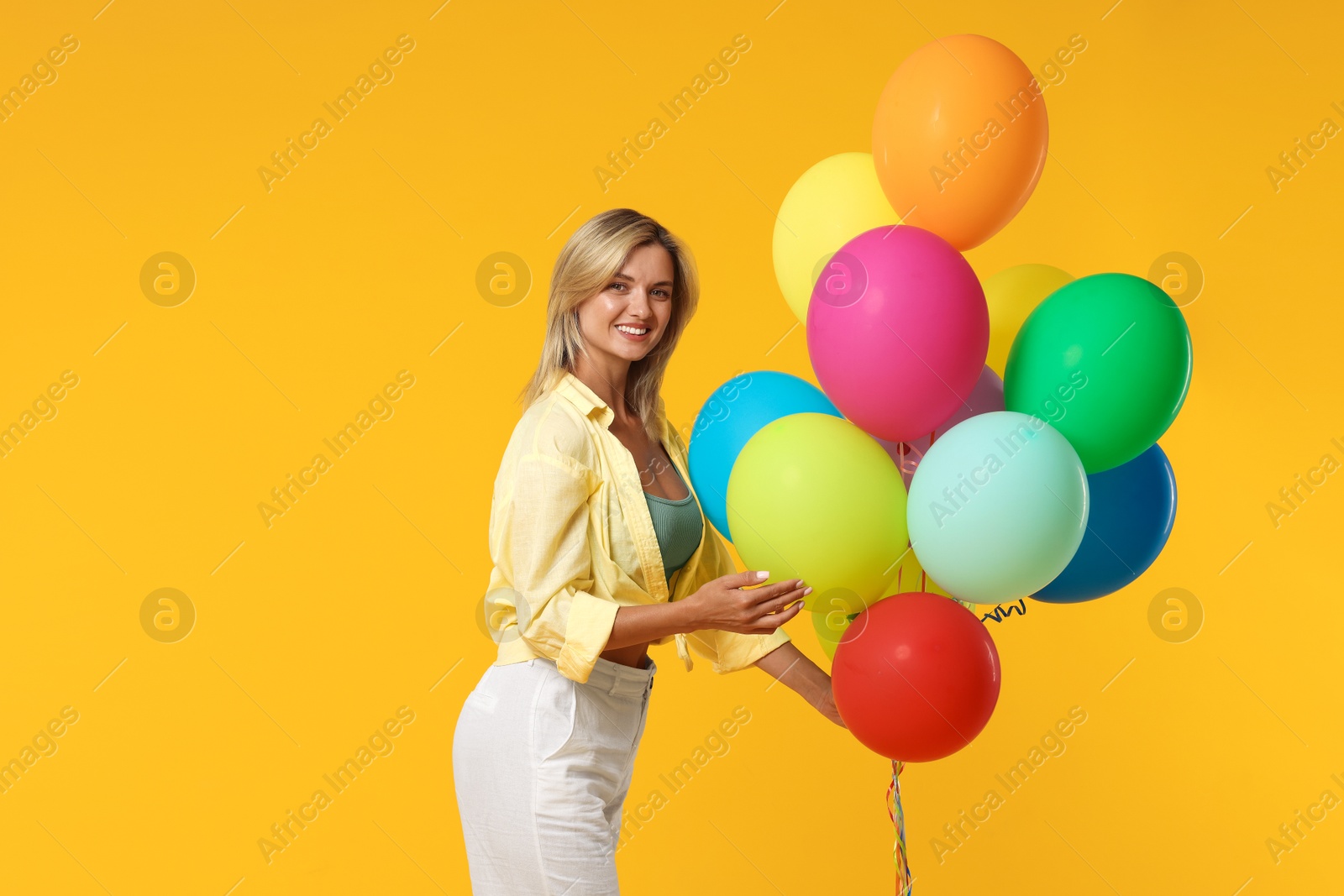 Happy woman with bunch of colorful balloons on yellow background Photo of Happy woman with bunch of colorful balloons on yellow background