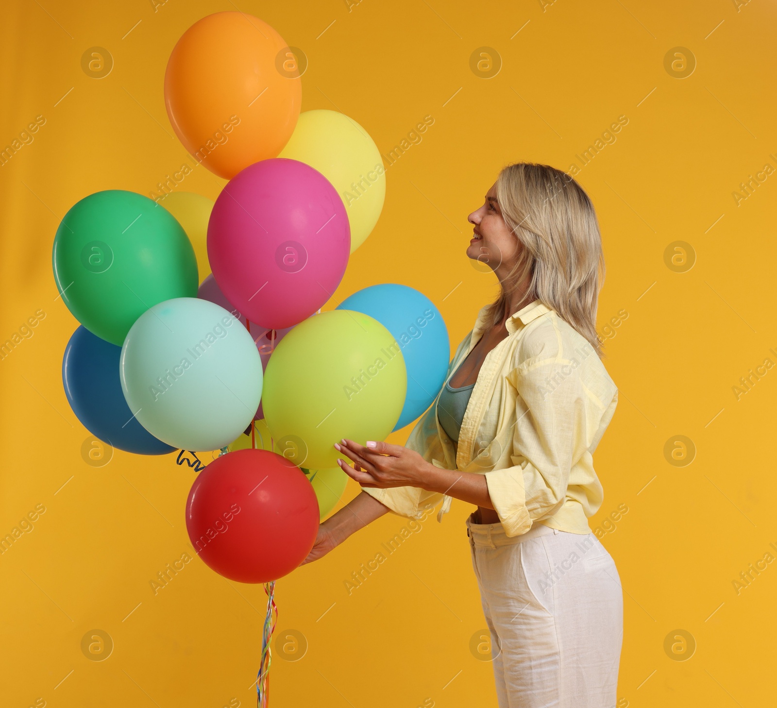 Happy woman with bunch of colorful balloons on yellow background Photo of Happy woman with bunch of colorful balloons on yellow background