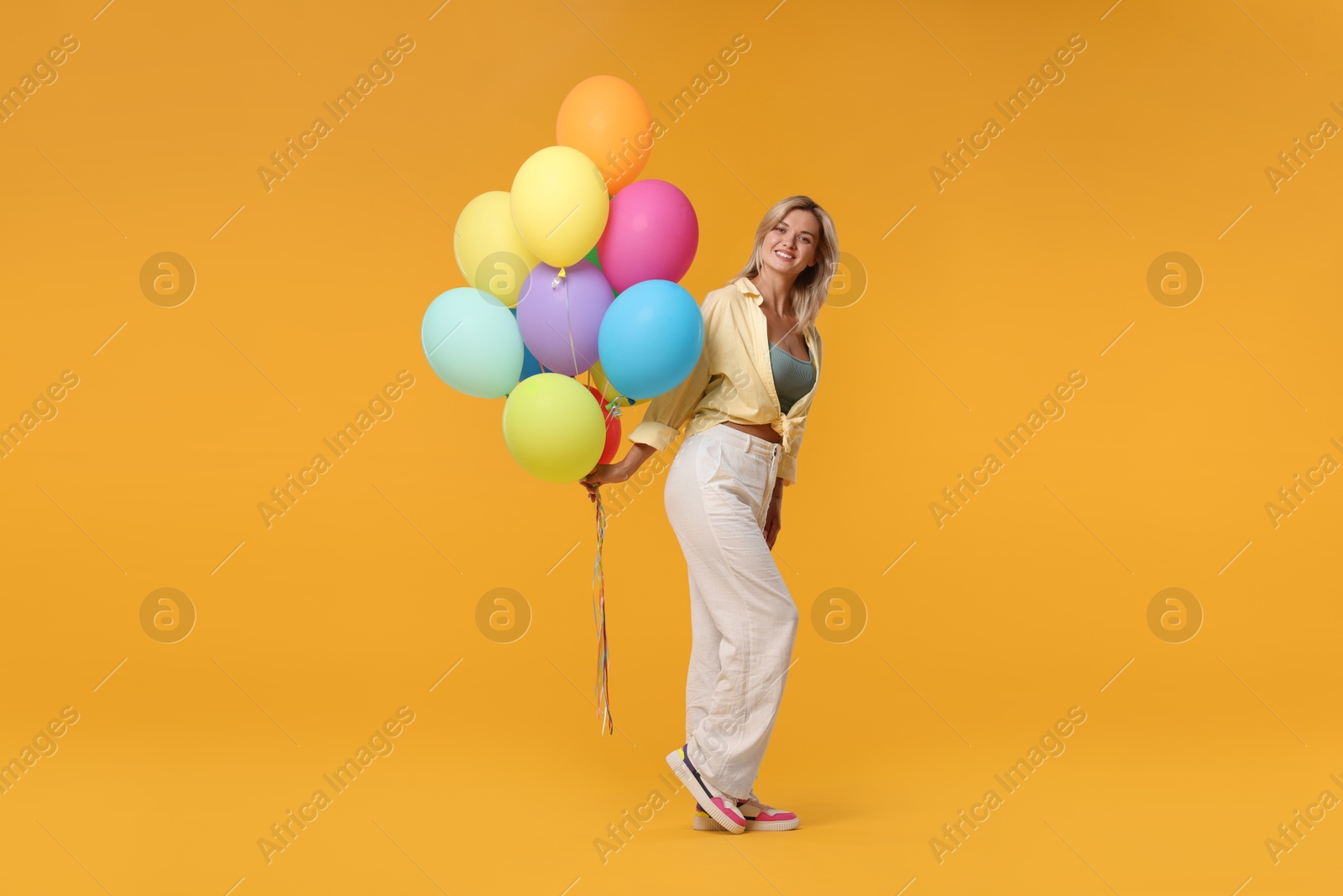 Photo of Happy woman with bunch of colorful balloons on yellow background