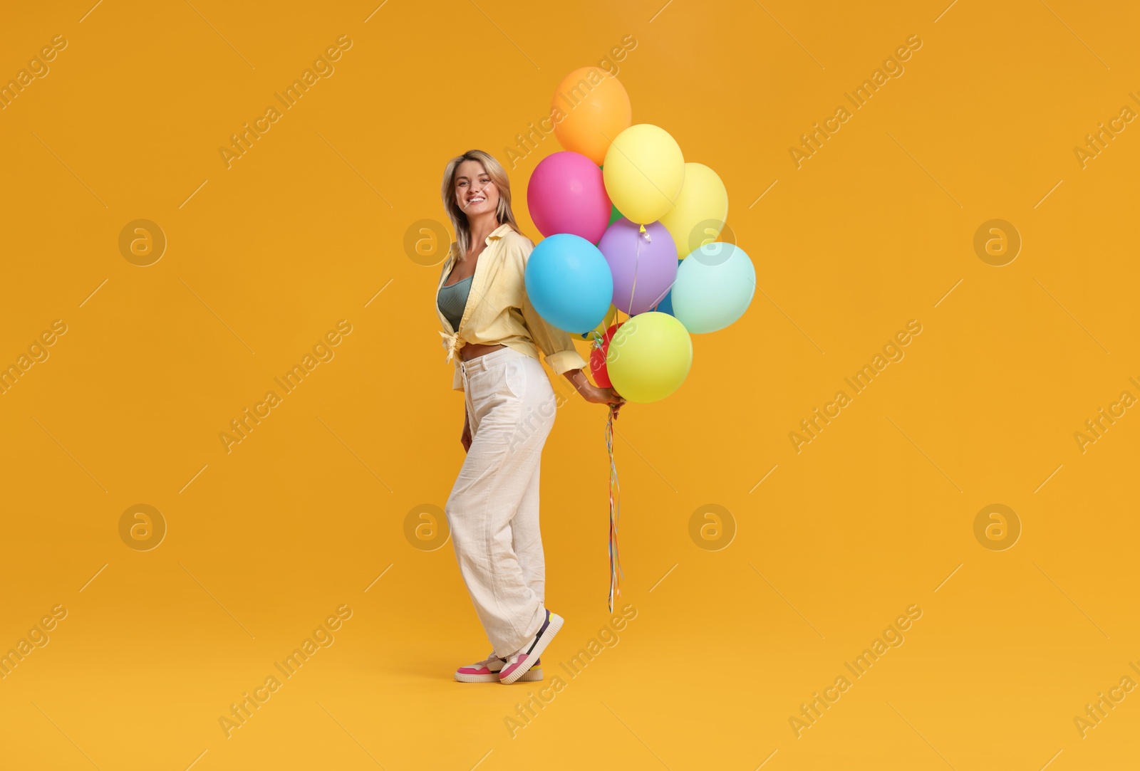 Photo of Happy woman with bunch of colorful balloons on yellow background
