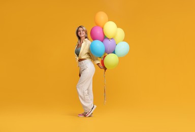 Photo of Happy woman with bunch of colorful balloons on yellow background