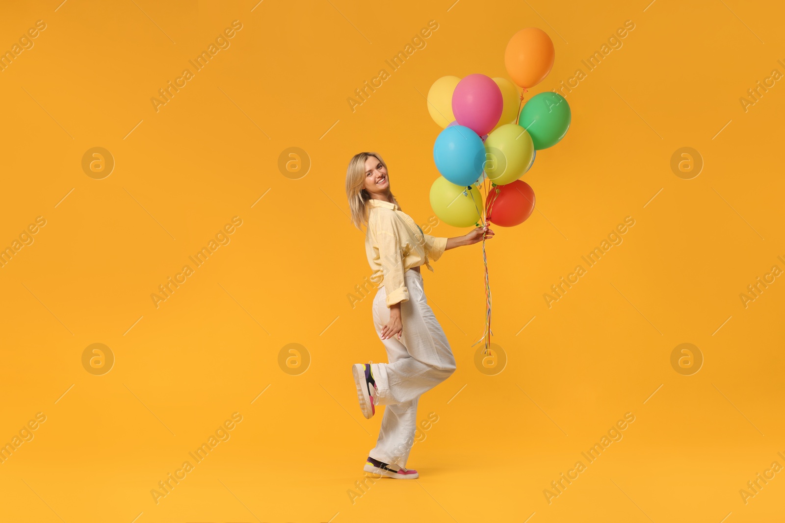 Photo of Happy woman with bunch of colorful balloons on yellow background