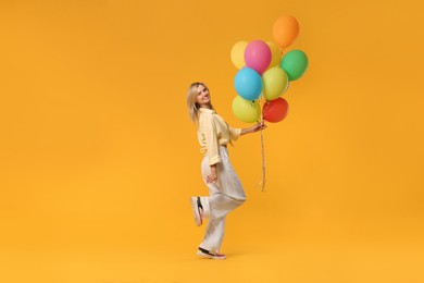 Photo of Happy woman with bunch of colorful balloons on yellow background