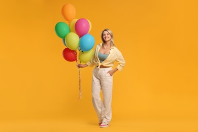 Photo of Happy woman with bunch of colorful balloons on yellow background