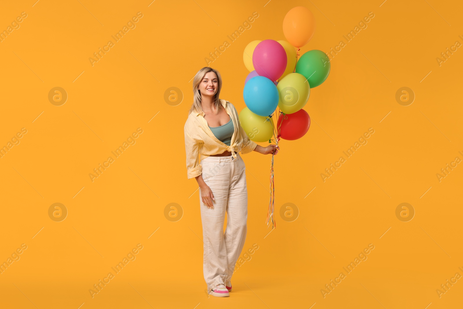 Photo of Happy woman with bunch of colorful balloons on yellow background