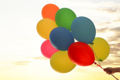 Photo of Woman with bunch of colorful balloons under beautiful sky at sunset, low angle view