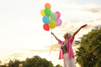 Photo of Smiling woman with bunch of colorful balloons under beautiful sky at sunset, low angle view. Space for text