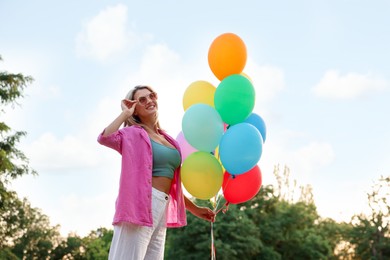 Photo of Smiling woman in sunglasses with bunch of colorful balloons outdoors, low angle view