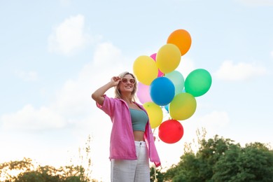 Photo of Smiling woman in sunglasses with bunch of colorful balloons outdoors, low angle view