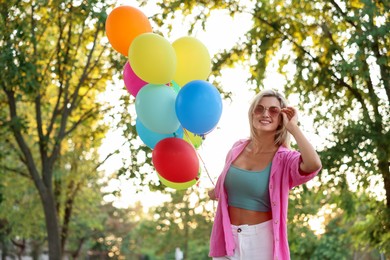 Photo of Smiling woman in sunglasses with bunch of colorful balloons outdoors