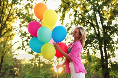 Photo of Smiling woman in sunglasses with bunch of colorful balloons outdoors