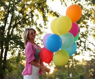 Photo of Smiling woman in sunglasses with bunch of colorful balloons outdoors