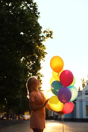 Photo of Smiling woman with bunch of colorful balloons outdoors at sunset