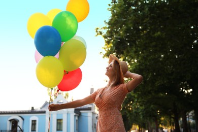 Photo of Smiling woman in hat with bunch of colorful balloons outdoors