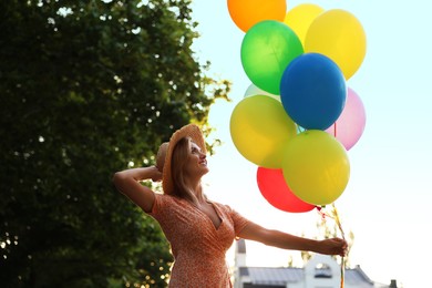 Photo of Smiling woman in hat with bunch of colorful balloons outdoors, low angle view