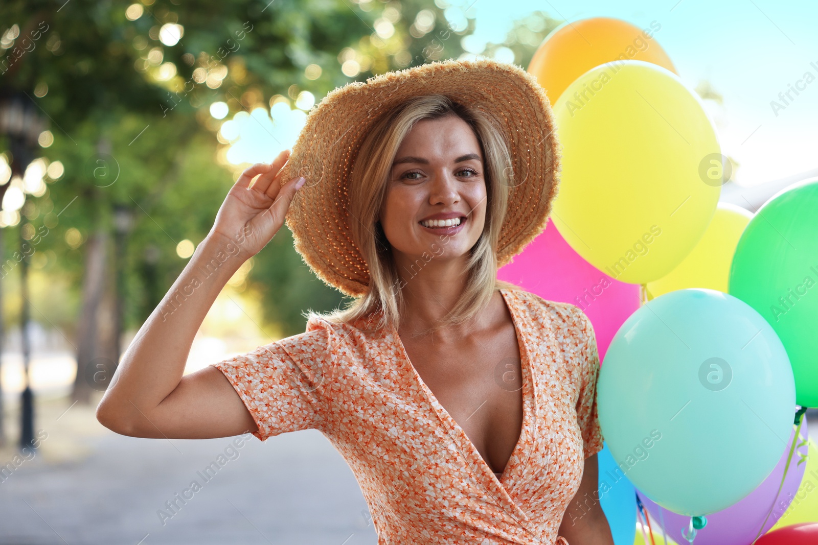Photo of Portrait of smiling woman in hat with bunch of colorful balloons outdoors
