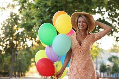 Photo of Portrait of smiling woman in hat with bunch of colorful balloons outdoors