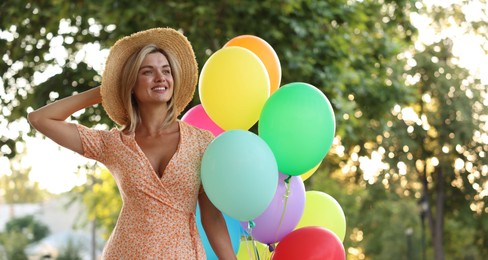 Photo of Smiling woman in hat with bunch of colorful balloons outdoors