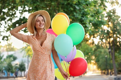 Photo of Smiling woman in hat with bunch of colorful balloons outdoors